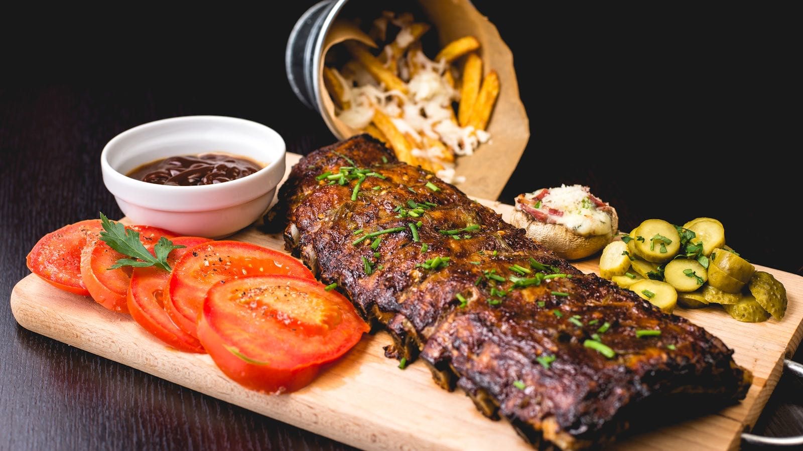 Costillas a la barbacoa con patatas, salsa y encurtidos servidas sobre una tabla de madera