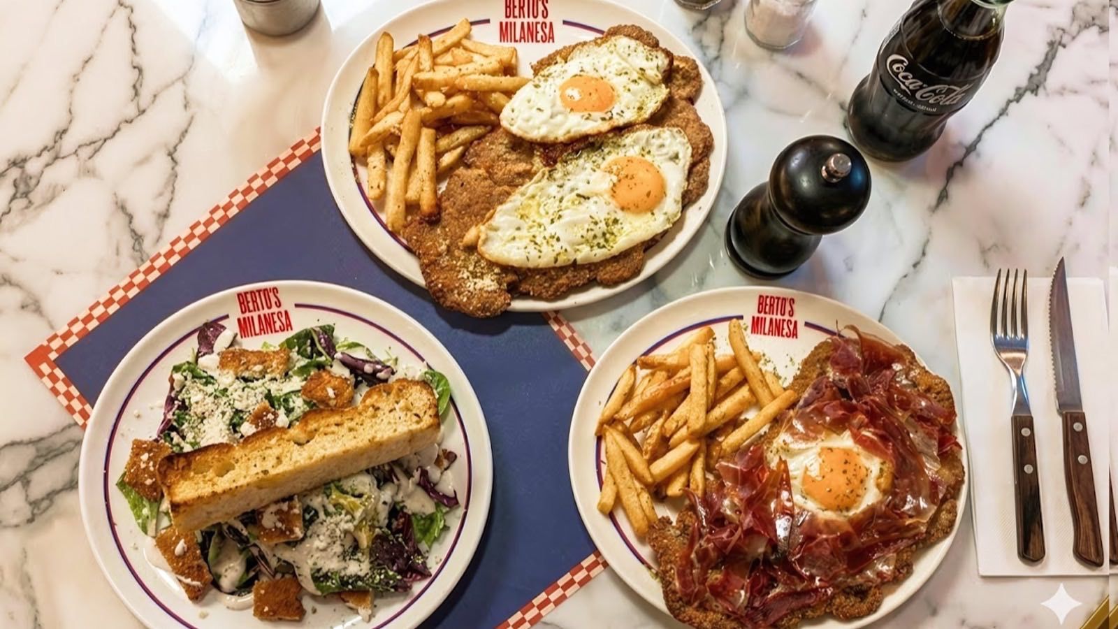 Tres platos de Berto's Milanesa sobre una mesa de mármol: milanesa con huevos y patatas, ensalada y milanesa con jamón