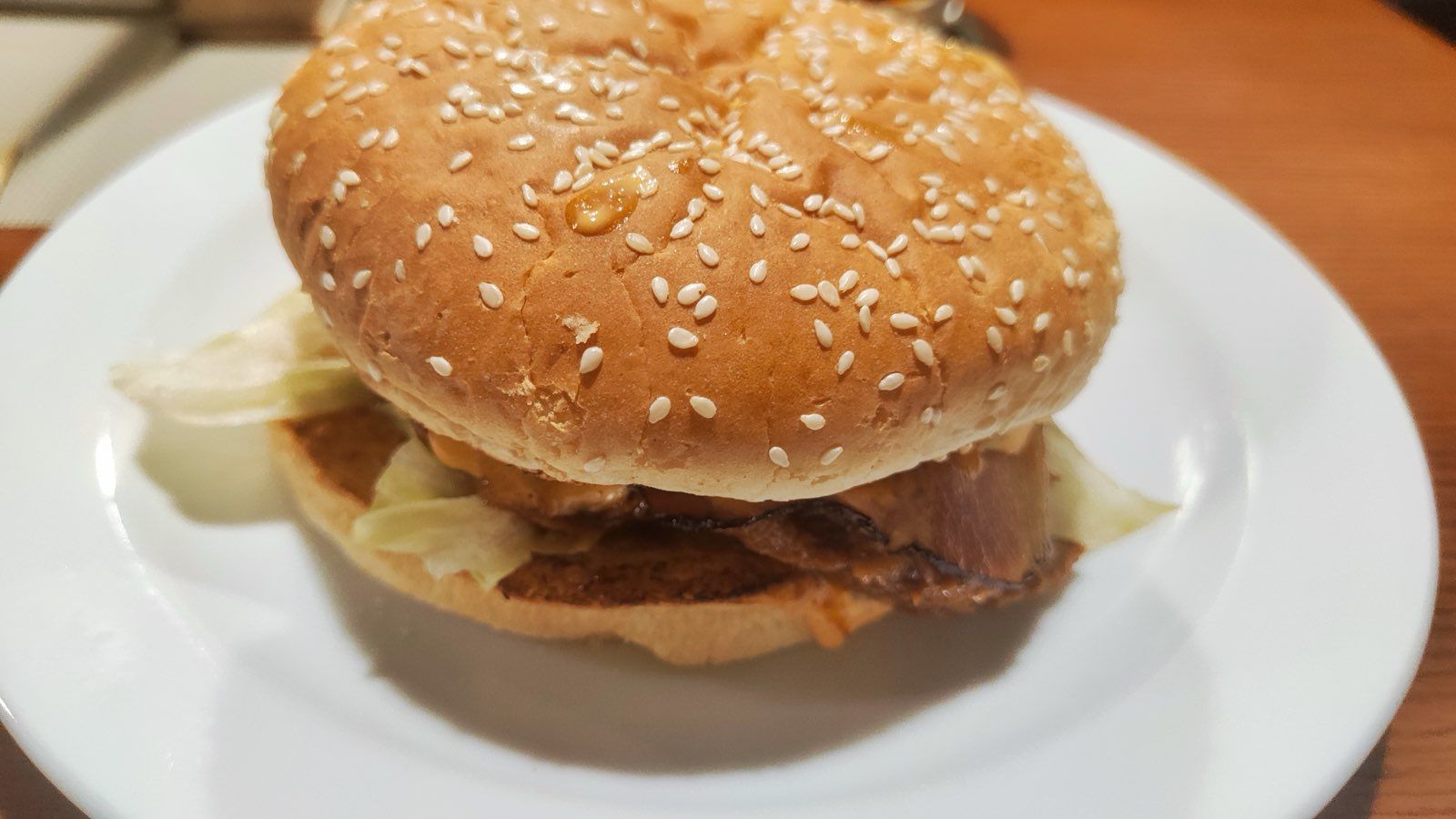 Hamburguesa con pan de sésamo, bacon y lechuga servida en un plato blanco sobre una mesa de restaurante