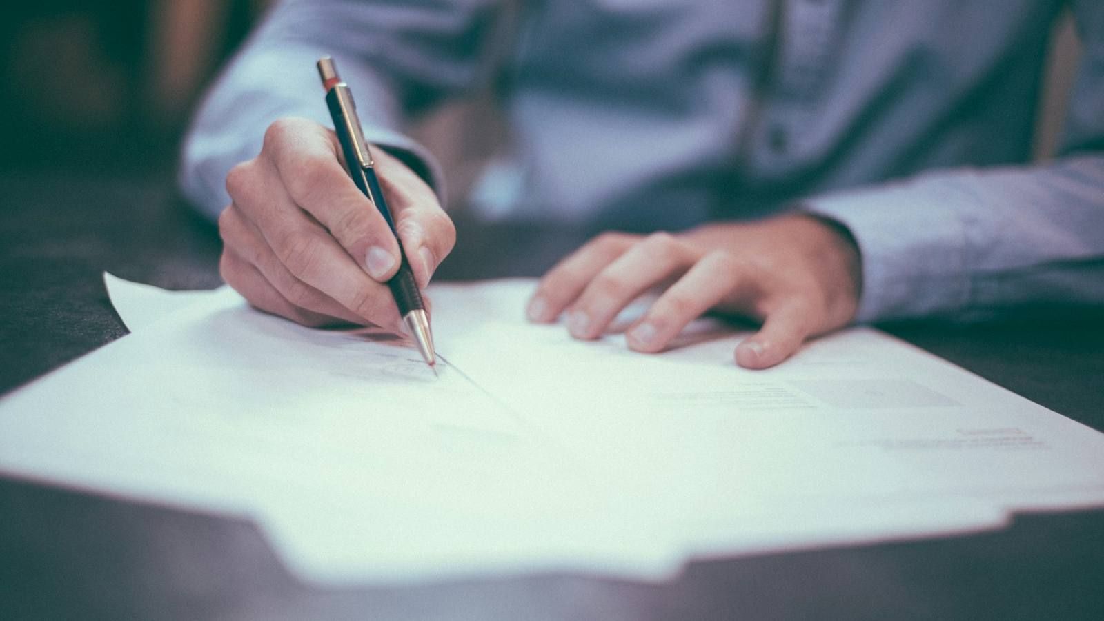 Mano firmando un contrato con una pluma sobre un escritorio
