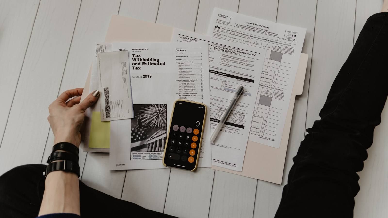 Persona revisando facturas con una calculadora sobre un escritorio blanco