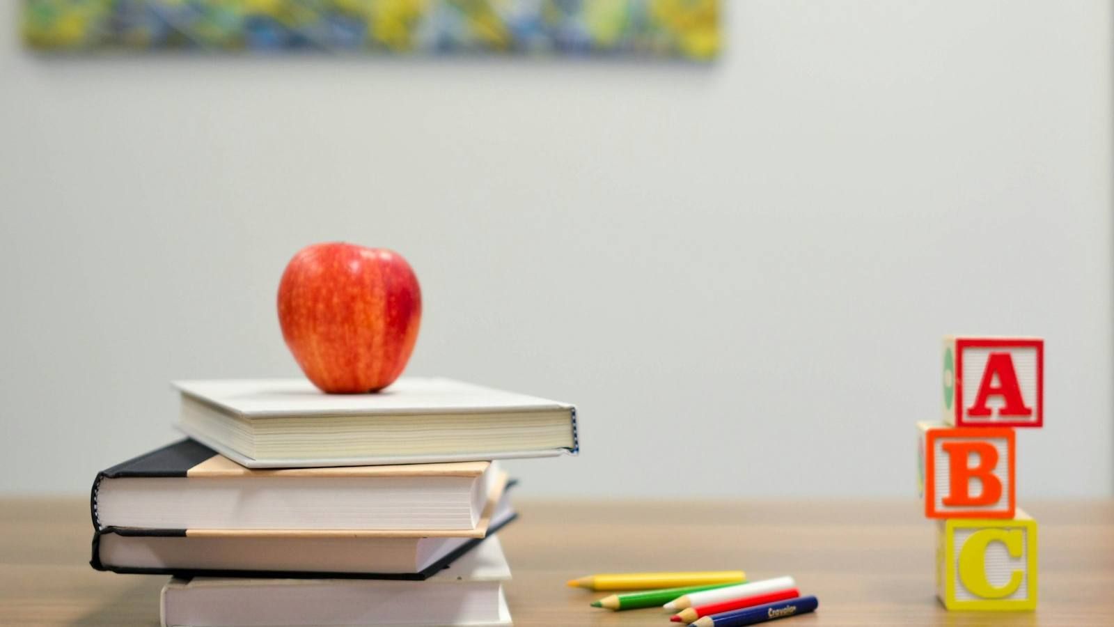 Libros apilados con una manzana y letras de juguete sobre un pupitre