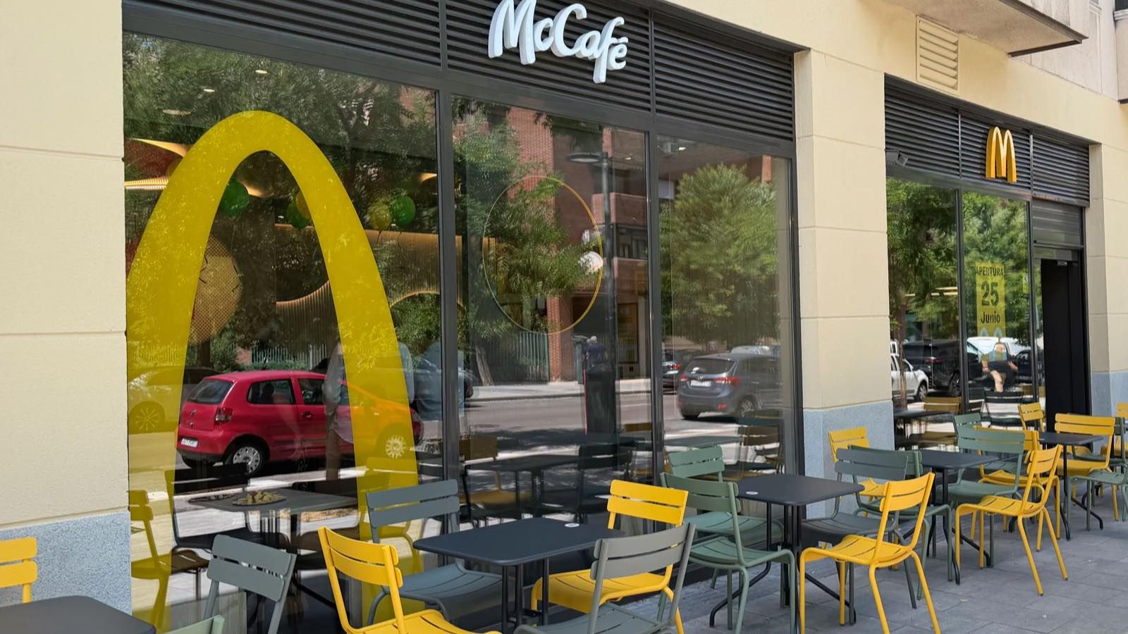 Terraza y fachada acristalada de un restaurante McDonald's recién inaugurado, con el arco dorado y un cartel de apertura en la ventana