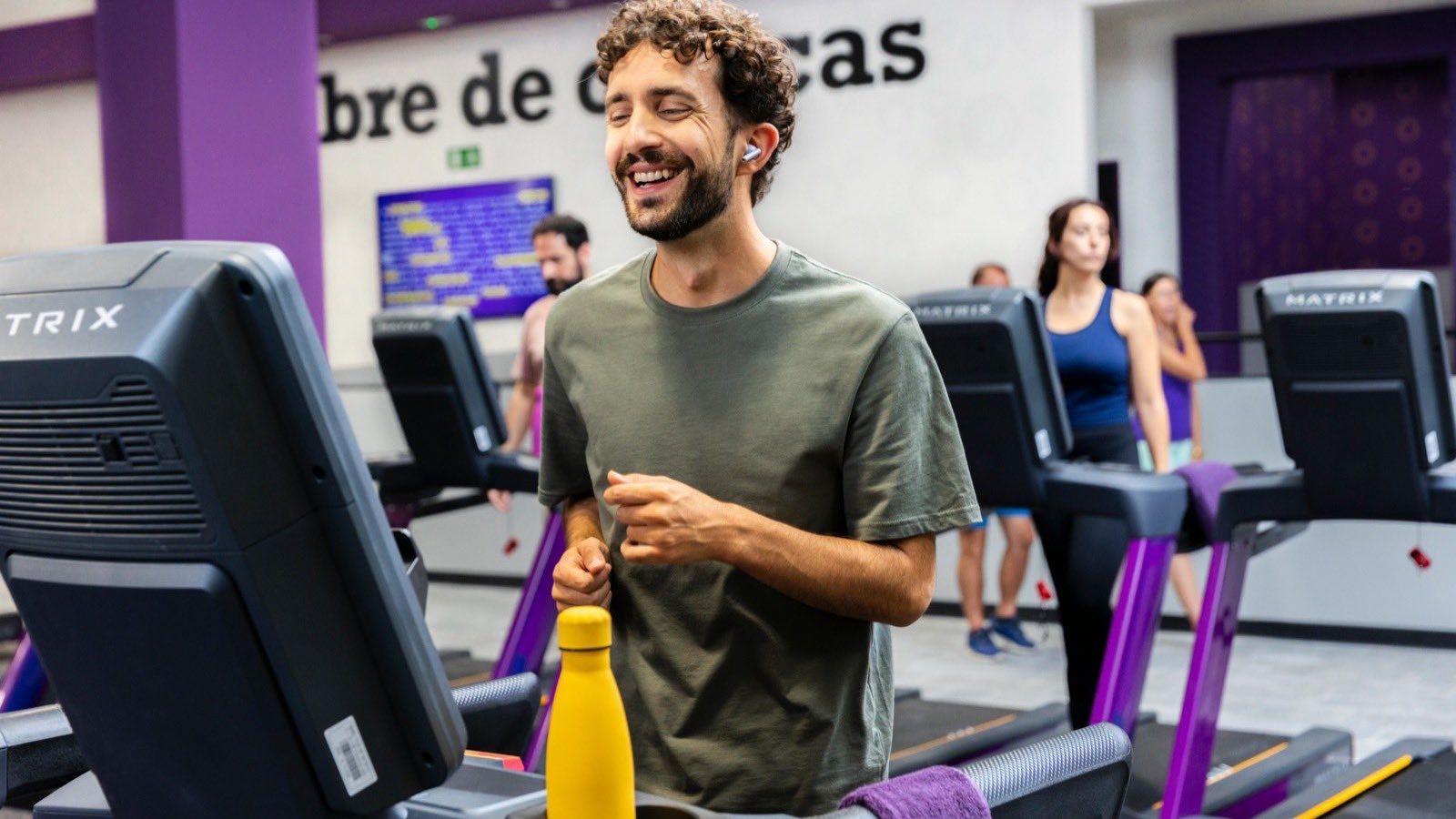 Socios entrenando en las cintas de correr de un club de Planet Fitness en España, frente al rótulo de la Zona Libre de Críticas