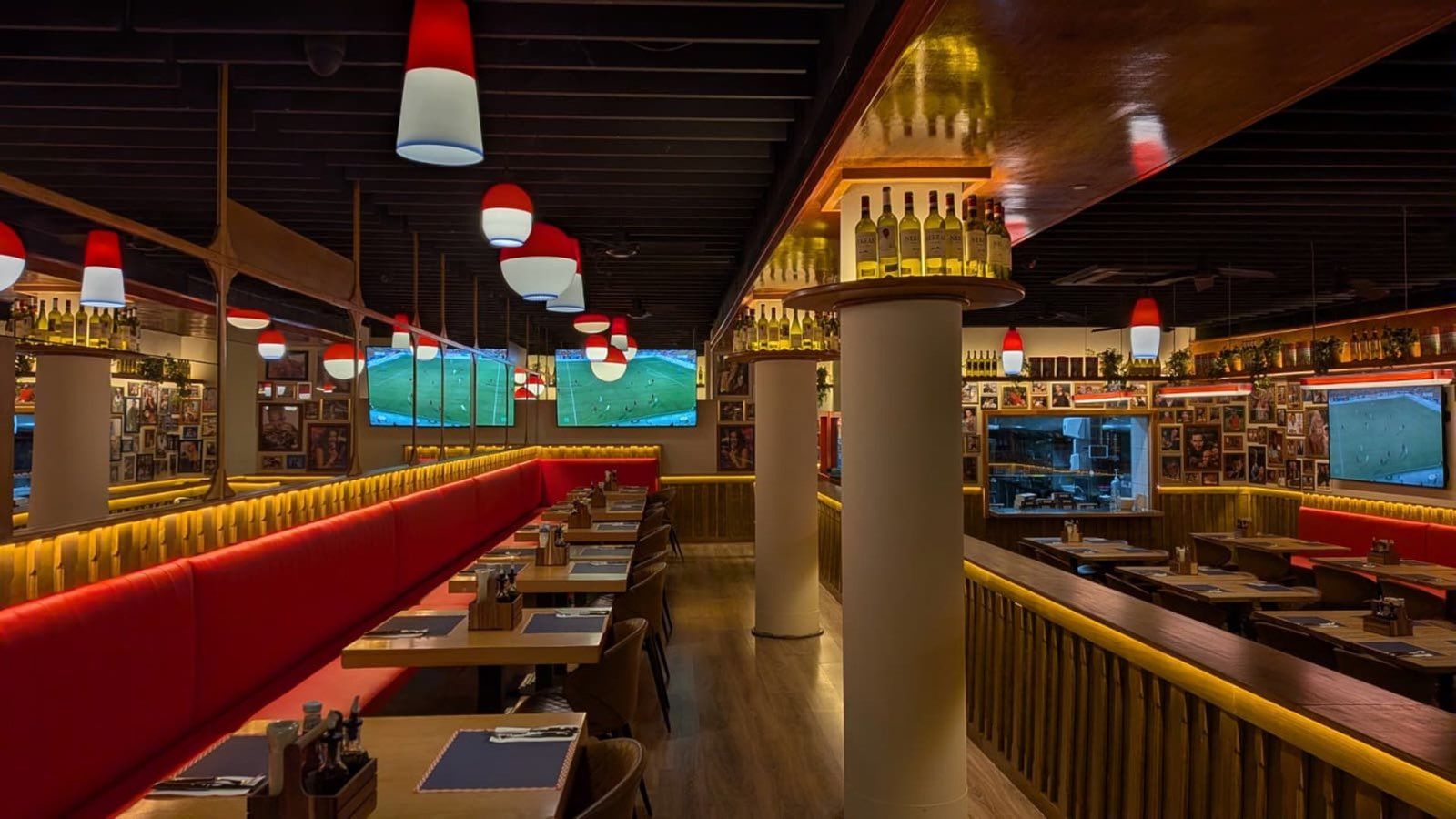 Comedor de un restaurante Berto's Milanesa, con bancos rojos, lámparas rojas y blancas y pantallas de fútbol
