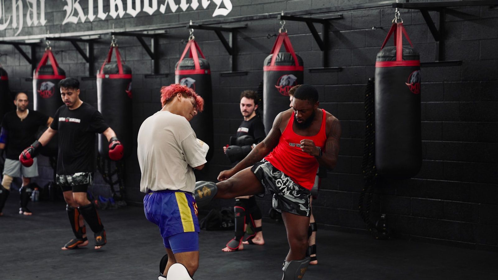 Alumnos de una clase de kickboxing entrenando por parejas junto a una hilera de sacos pesados colgados de la pared de un gimnasio de deportes de contacto